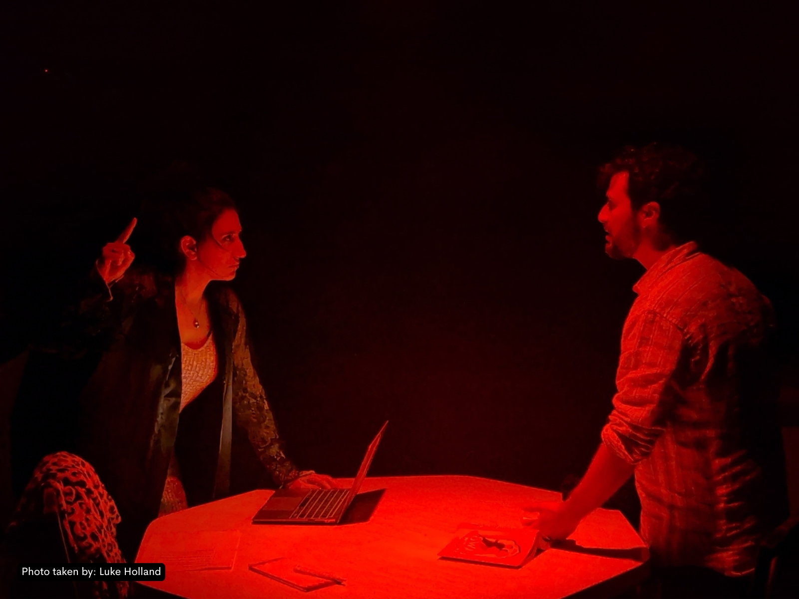 Two-shot mid-scene — emotional beat between Amaliah and Kaveh, faces close, hands on documents.